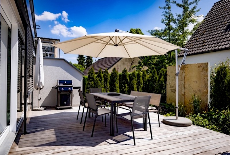 Holzterrasse mit Sitzgruppe und Sonnenschirm hinter einem Wohnhaus