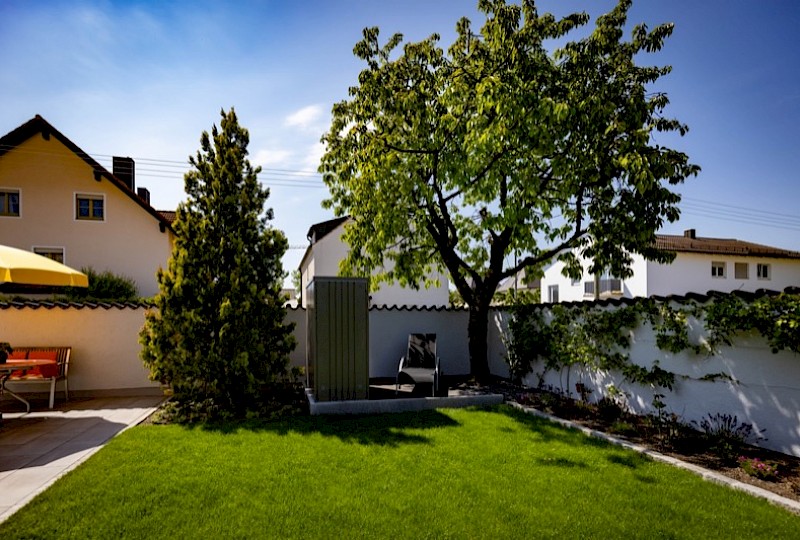 Gepflegter Rasen mit altem Baum, weißer Mauer und Sitzplatz