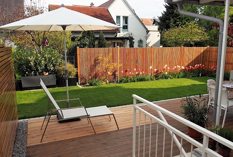 Holzlattenzaun als Sichtschutz mit Tulpenbeet, Rollrasen und Holzterrasse